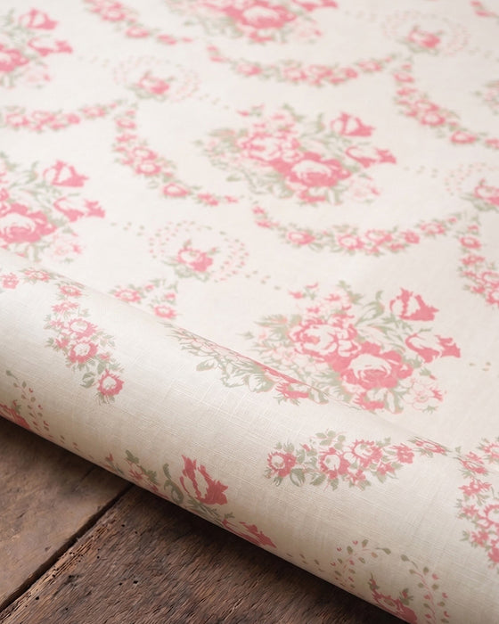 Roll of floral wallpaper with pink flowers on a wooden surface