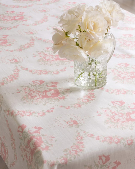 Floral arrangement in a glass vase on a pink and white floral tablecloth.