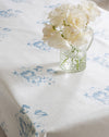 White flowers in a clear vase on a tablecloth with blue floral patterns