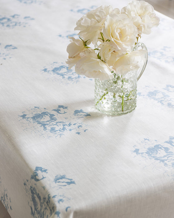 White flowers in a clear vase on a tablecloth with blue floral patterns