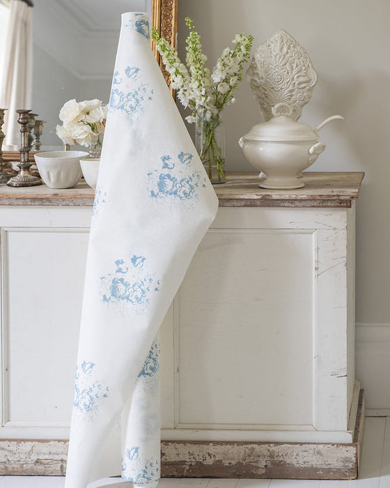 White towel with blue floral pattern draped over a wooden cabinet in a room with decorative items.