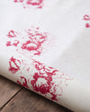 Roll of white fabric with red floral patterns on a wooden surface