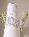 White vase with black floral patterns against a blurred floral background