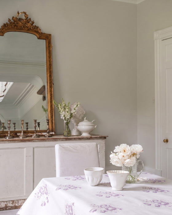 Dining room with a table set with white dishes and flowers, an ornate mirror on the wall.