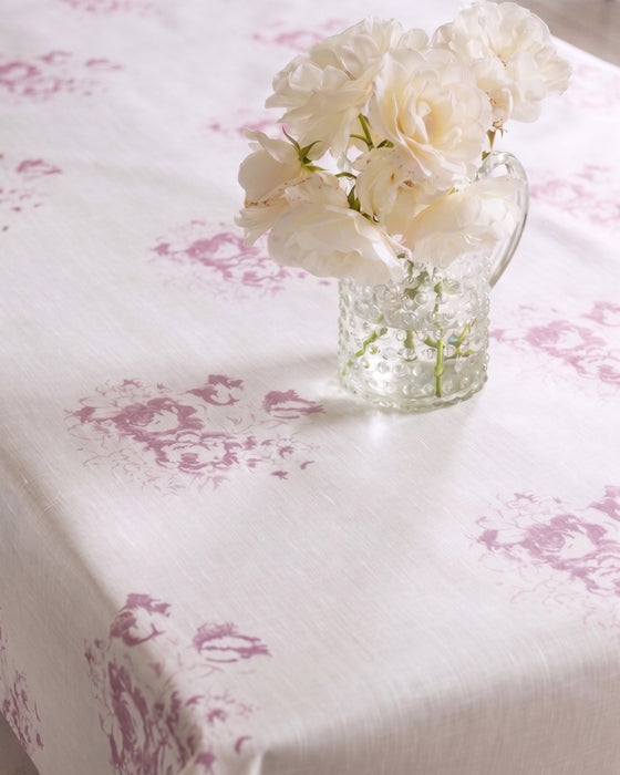 Tablecloth with floral pattern and a vase of white flowers on a table.