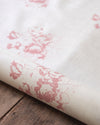 Roll of white fabric with pink floral pattern on a wooden surface