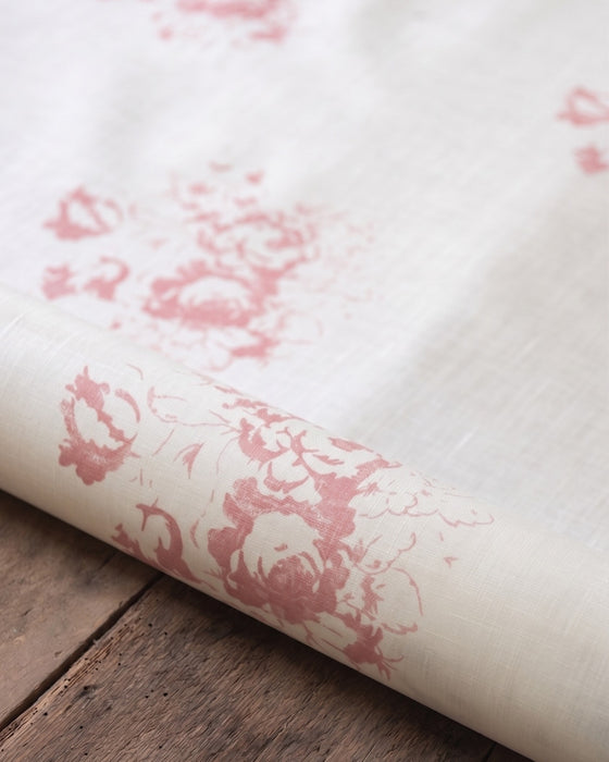Roll of white fabric with pink floral pattern on a wooden surface