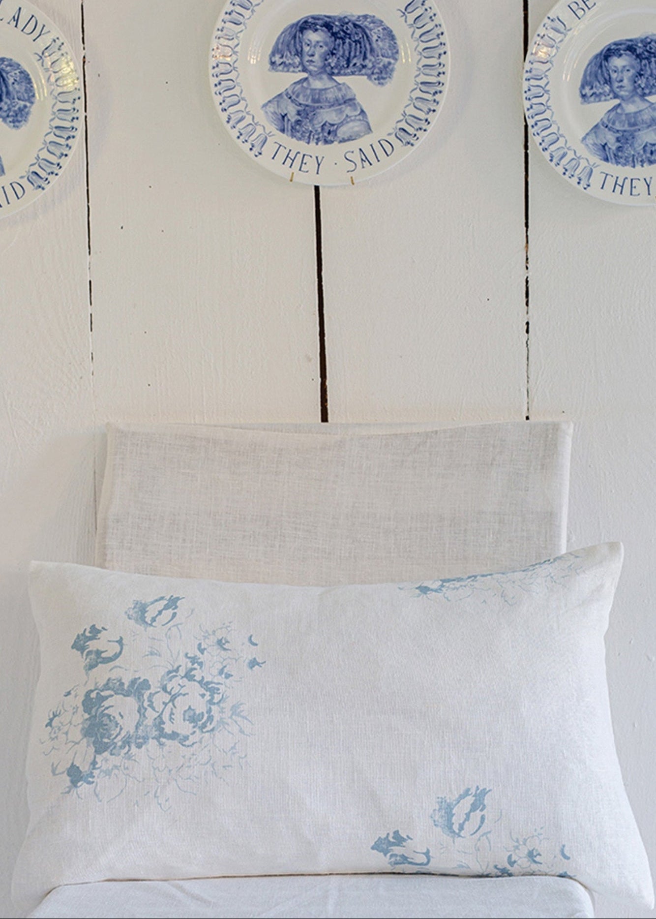 Decorative pillows with blue floral patterns on a wooden wall with circular blue and white decorative plates.